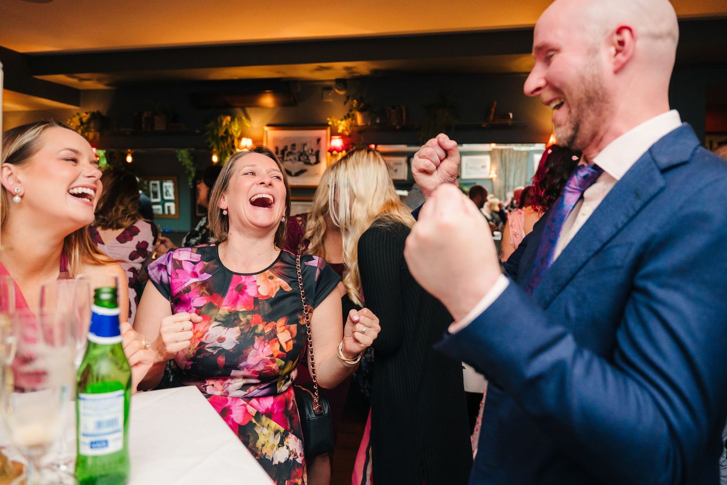 Party guests share laughs over drinks in a lively restaurant atmosphere. Marco Pierre Dublin Wedding Photographer