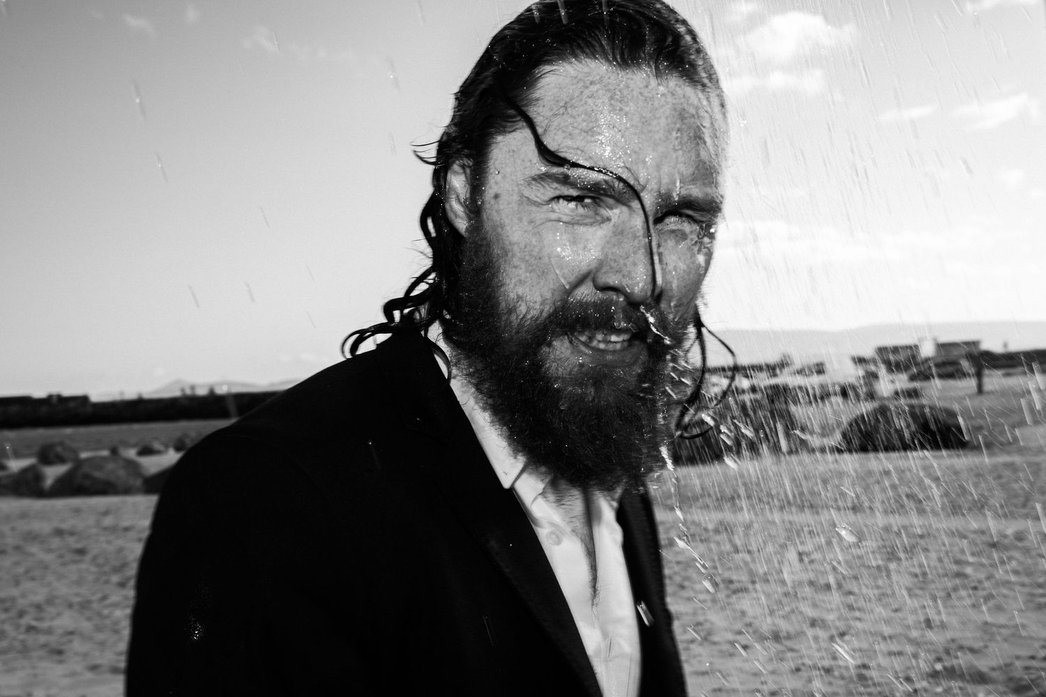 Black and white portrait of a bearded man with intense expression in a rural landscape setting. PHOTOGRAPHER Dublin