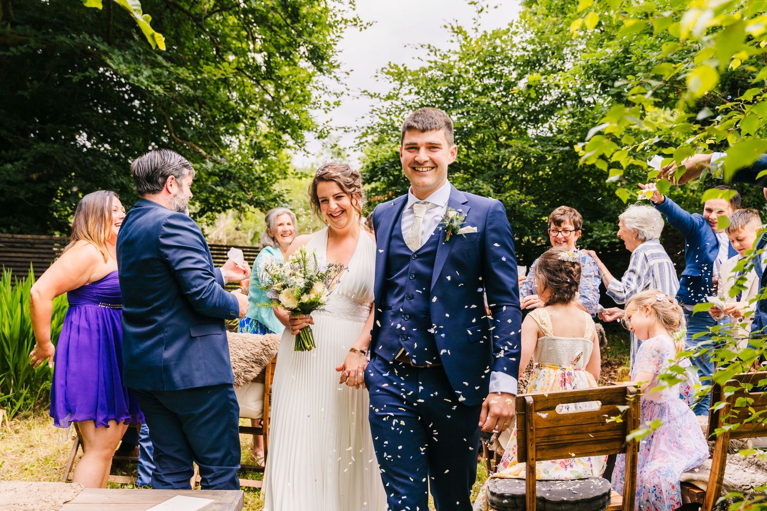 Wedding guests throw blue confetti over a happy couple during an outdoor garden ceremony. Wedding PHOTOGRAPHER Dublin