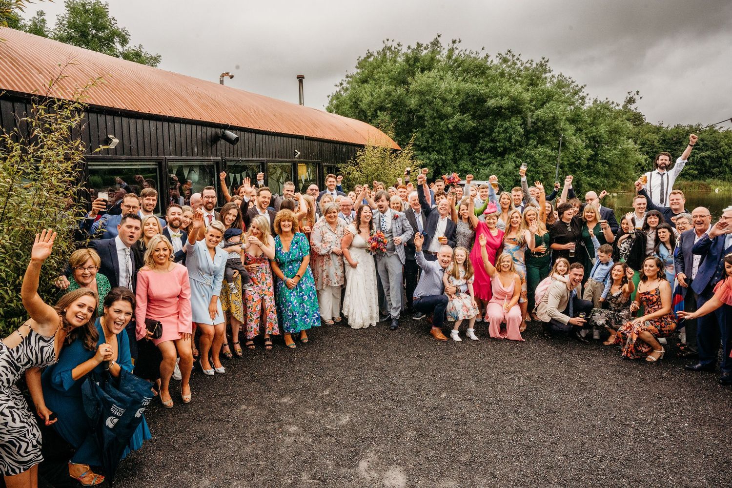 Panoramic shot of wedding guests gathered outside a rustic venue. Wedding photographer Dublin