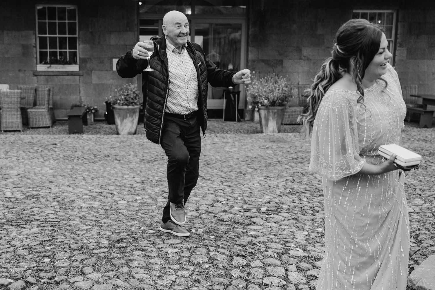 A black and white photo showing wedding guests dancing on a cobblestone courtyard. wedding photographer dublin