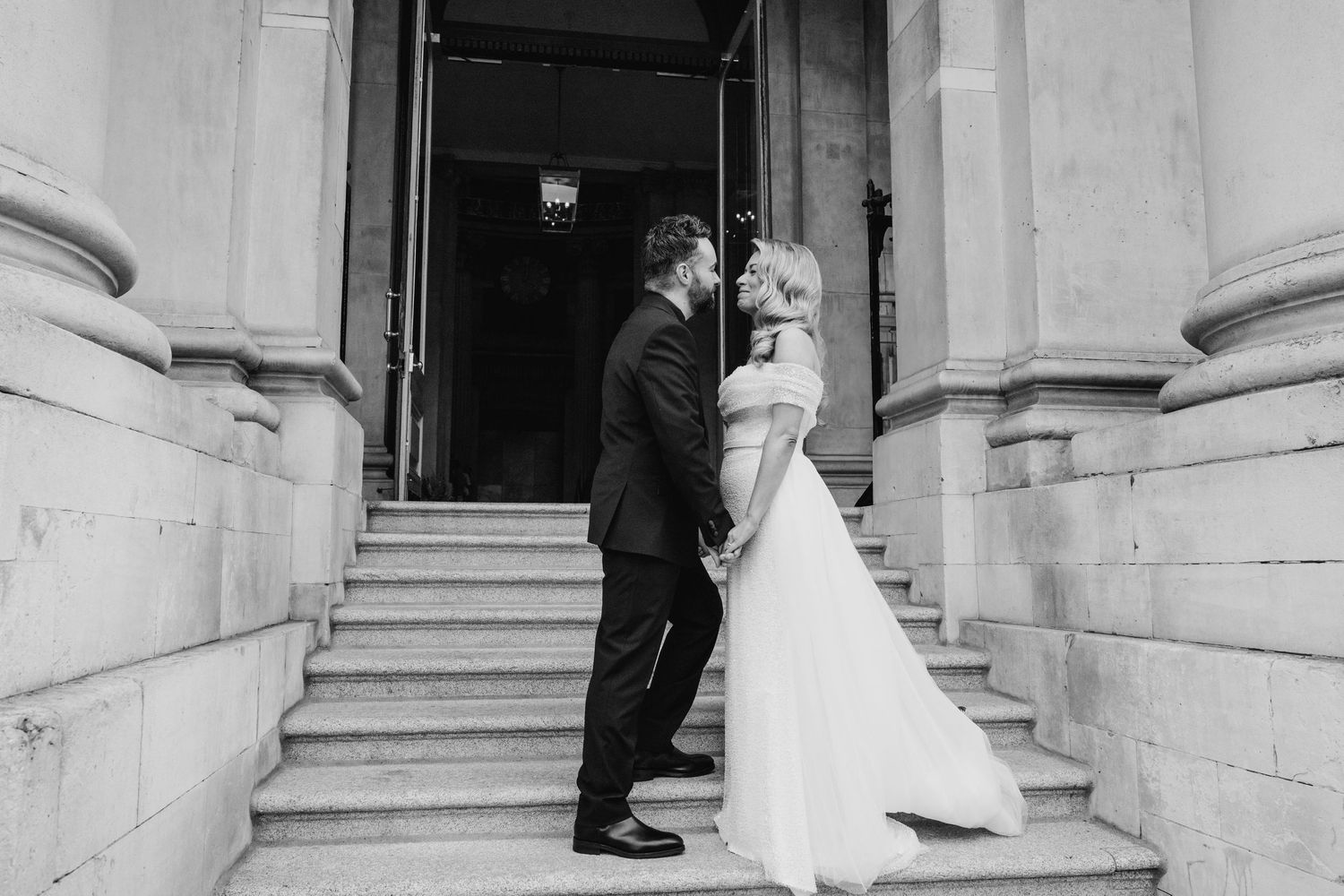 Black and white photo of couple embracing on stone steps between classical columns.  city hall dublin wedding photos