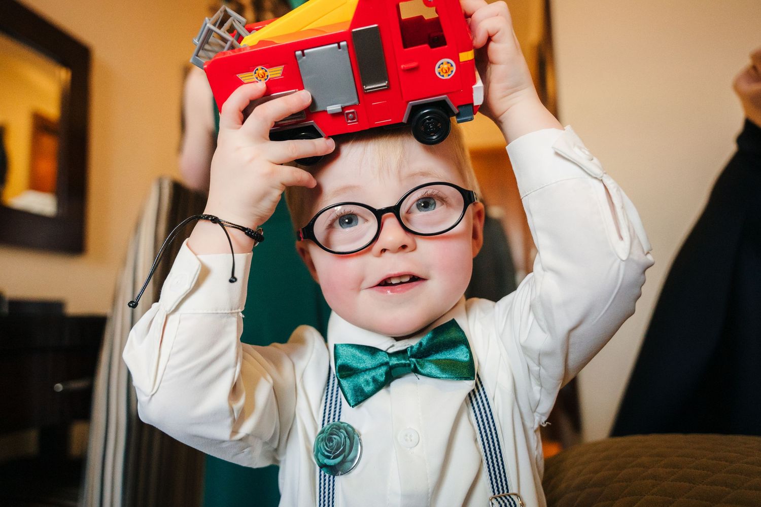 Young child in formal wear plays with a red toy truck during a wedding event.  Wedding PHOTOGRAPHER Trim Castle