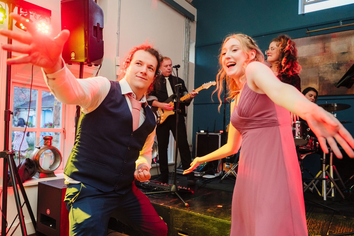 A couple dancing energetically at a wedding reception with a band performing in the background. . Village Barn Tyrrellspass wedding photogra