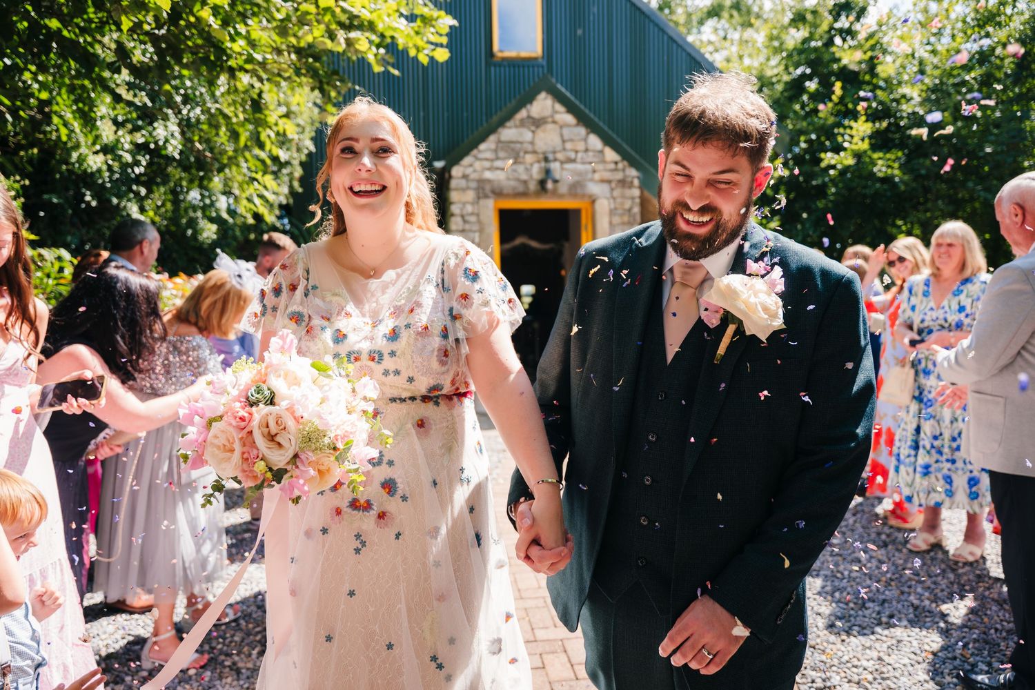 Happy newlyweds walk through a shower of confetti outside a charming blue chapel. . Village Barn Tyrrellspass wedding photographer Ireland