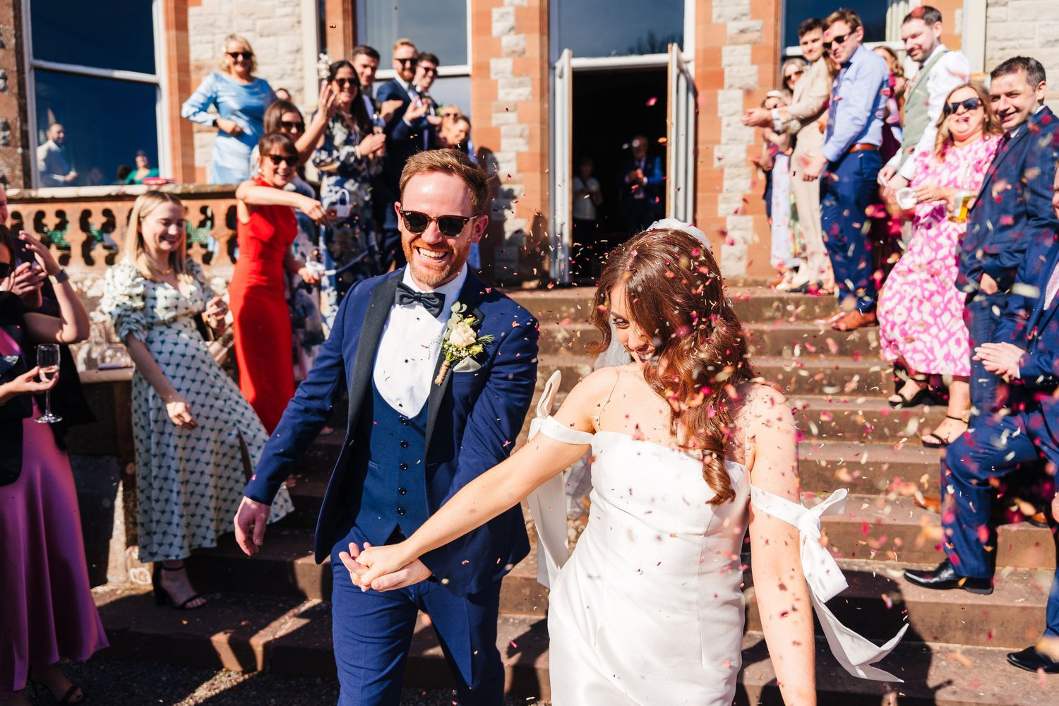 Castle Leslie Wedding Photographer Dublin Wedding guests celebrating with confetti and flower petals in front of historic brick building.