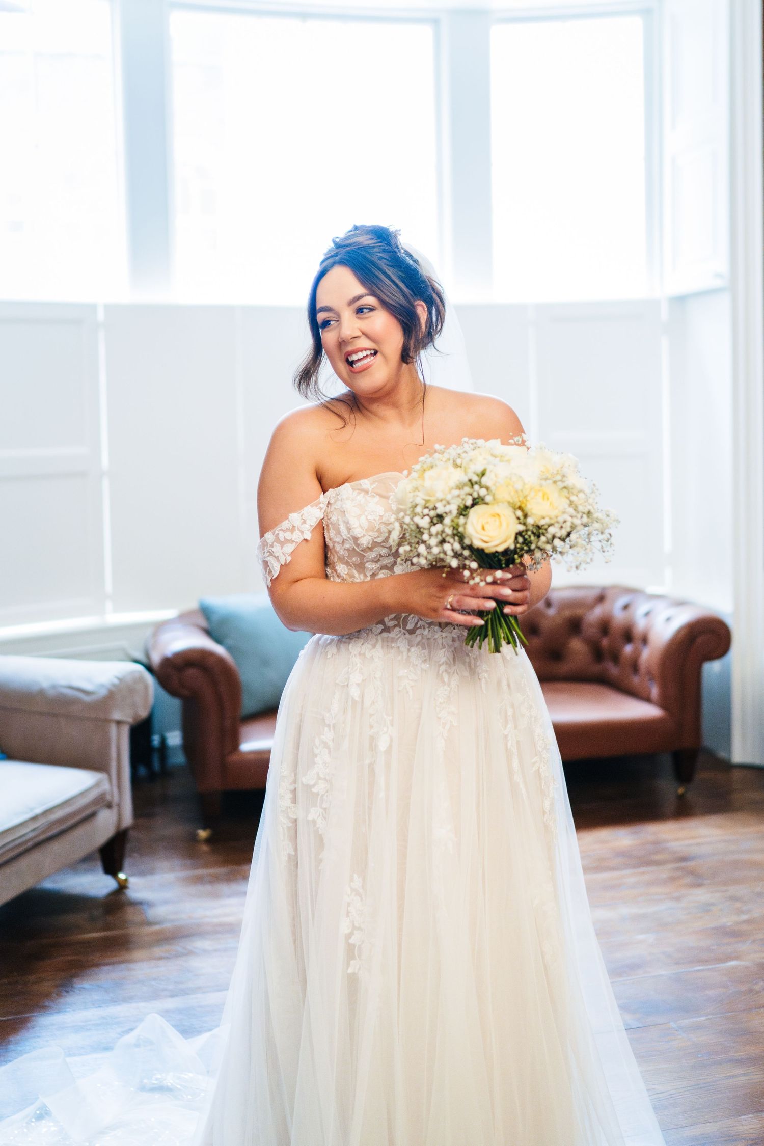 A wedding dress is showcased in an elegant room with large windows and a leather couch.  Wedding PHOTOGRAPHER Dublin