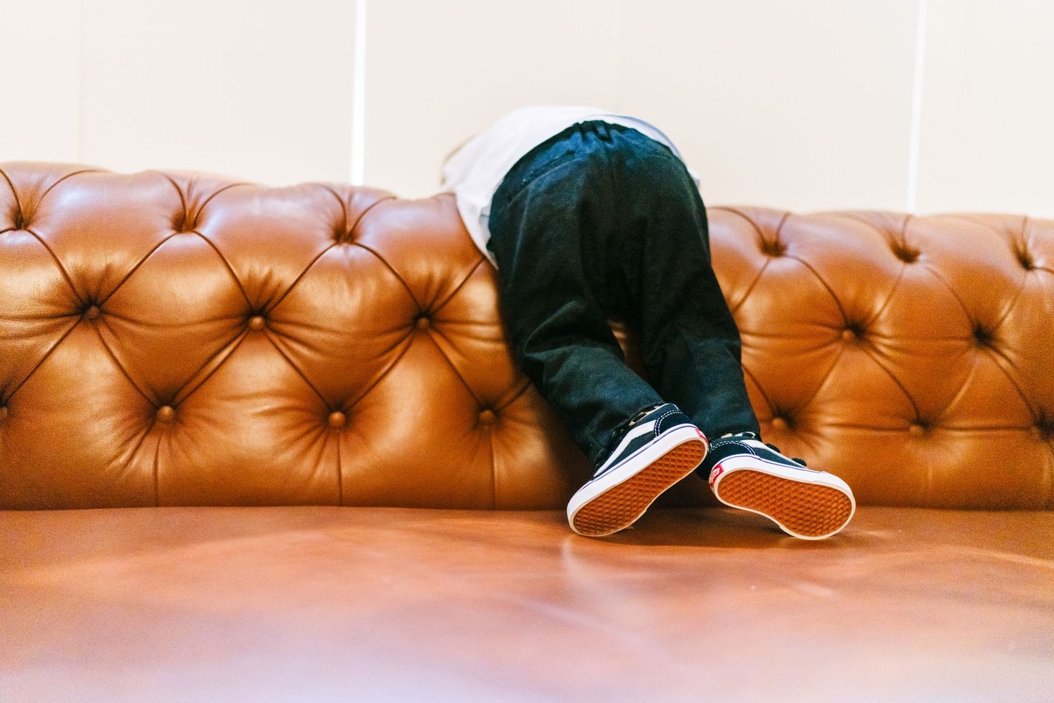 A person lies face down on a brown leather tufted couch wearing dark pants and sneakers. Wedding PHOTOGRAPHER Dublin