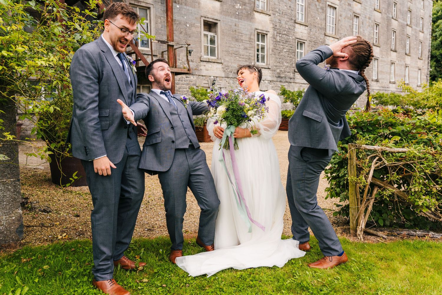 Millhouse slane wedding photographer dublin Wedding party members pose playfully on the lawn of a historic stone building.