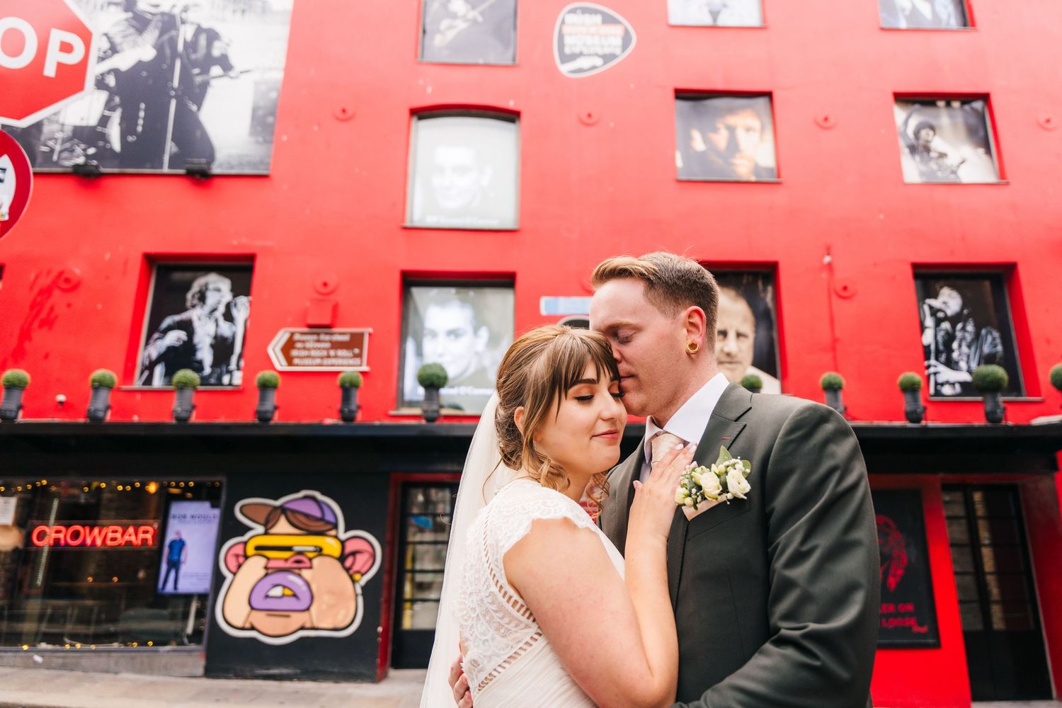 Intimate moment between newlyweds against red wall decorated with vintage photographs. PHOTOGRAPHER Dublin Ireland Wedding