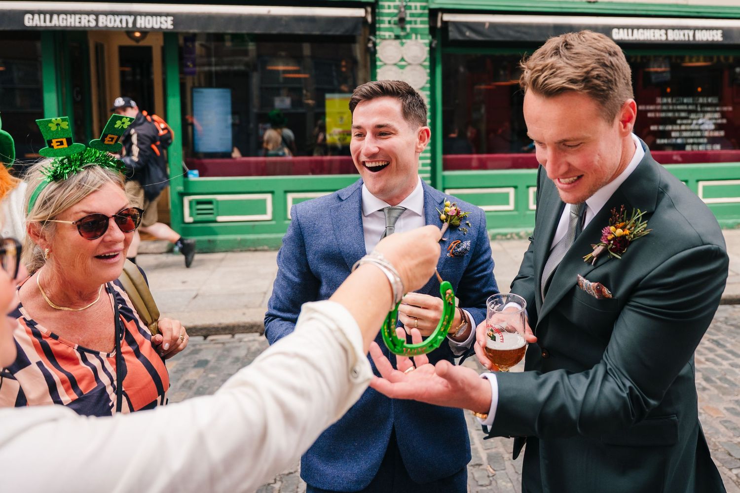Wedding party members share drinks and laugh together outside a green-fronted pub. Same sex wedding PHOTOGRAPHER Dublin