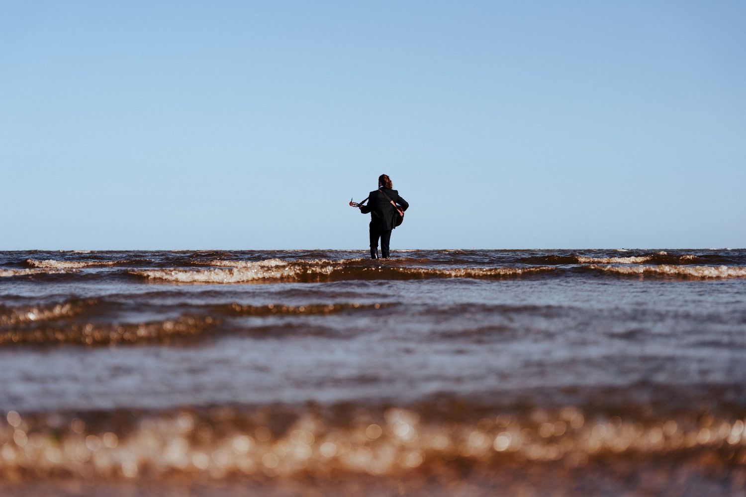 A silhouetted figure walks across a vast, shallow mudflat at sunset with reflective water. PHOTOGRAPHER Dublin