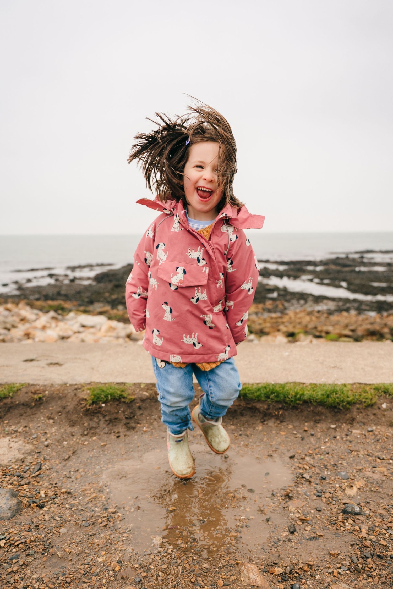 A series of photos showing joyful moments at a rocky beach in a pink patterned sweater and jeans. PHOTOGRAPHER Dublin