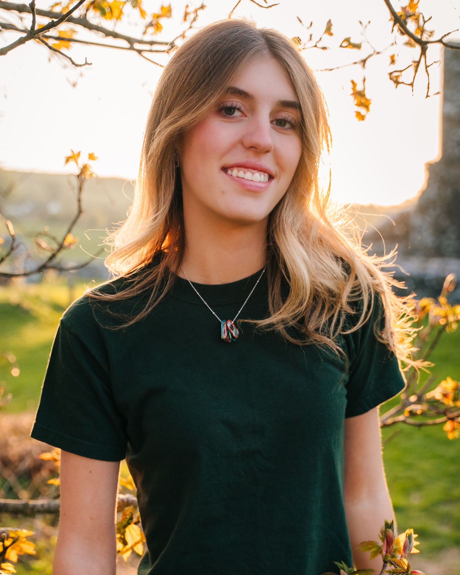 Person in a dark green shirt smiling in front of autumn trees during golden hour. Photographer Ireland dublin