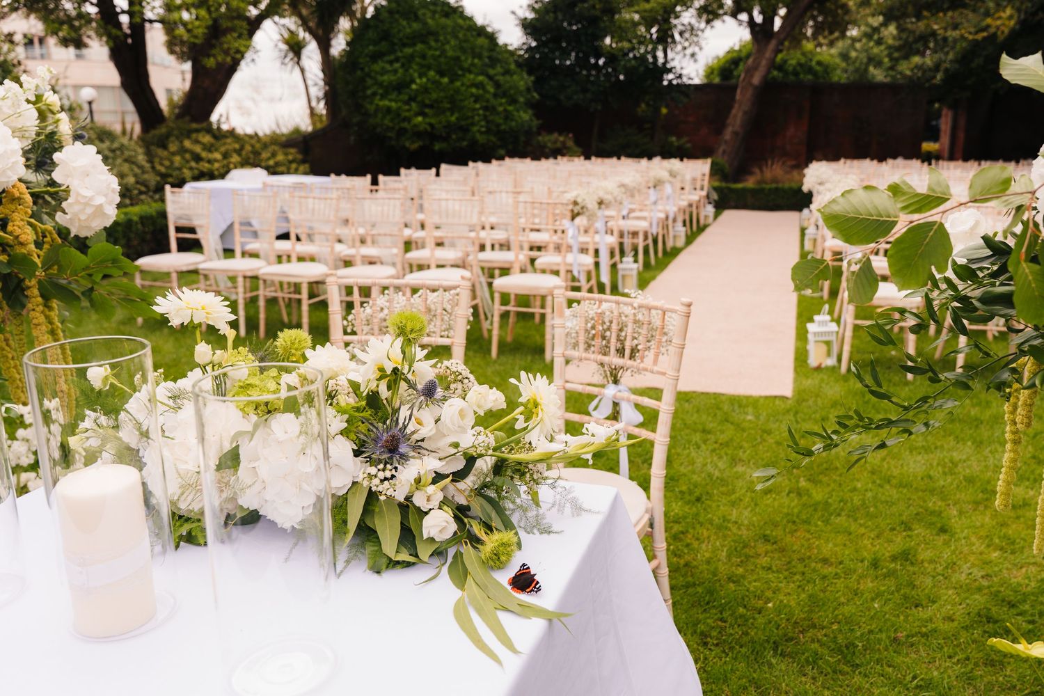 Outdoor wedding venue setup with white chairs and floral arrangements in a garden setting. Portmarnock Hotel Wedding PHOTOGRAPHER Dublin