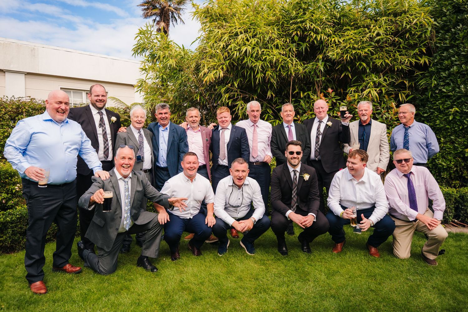 Wedding party guests pose together on grass against a backdrop of greenery. Portmarnock Hotel Wedding PHOTOGRAPHER Dublin
