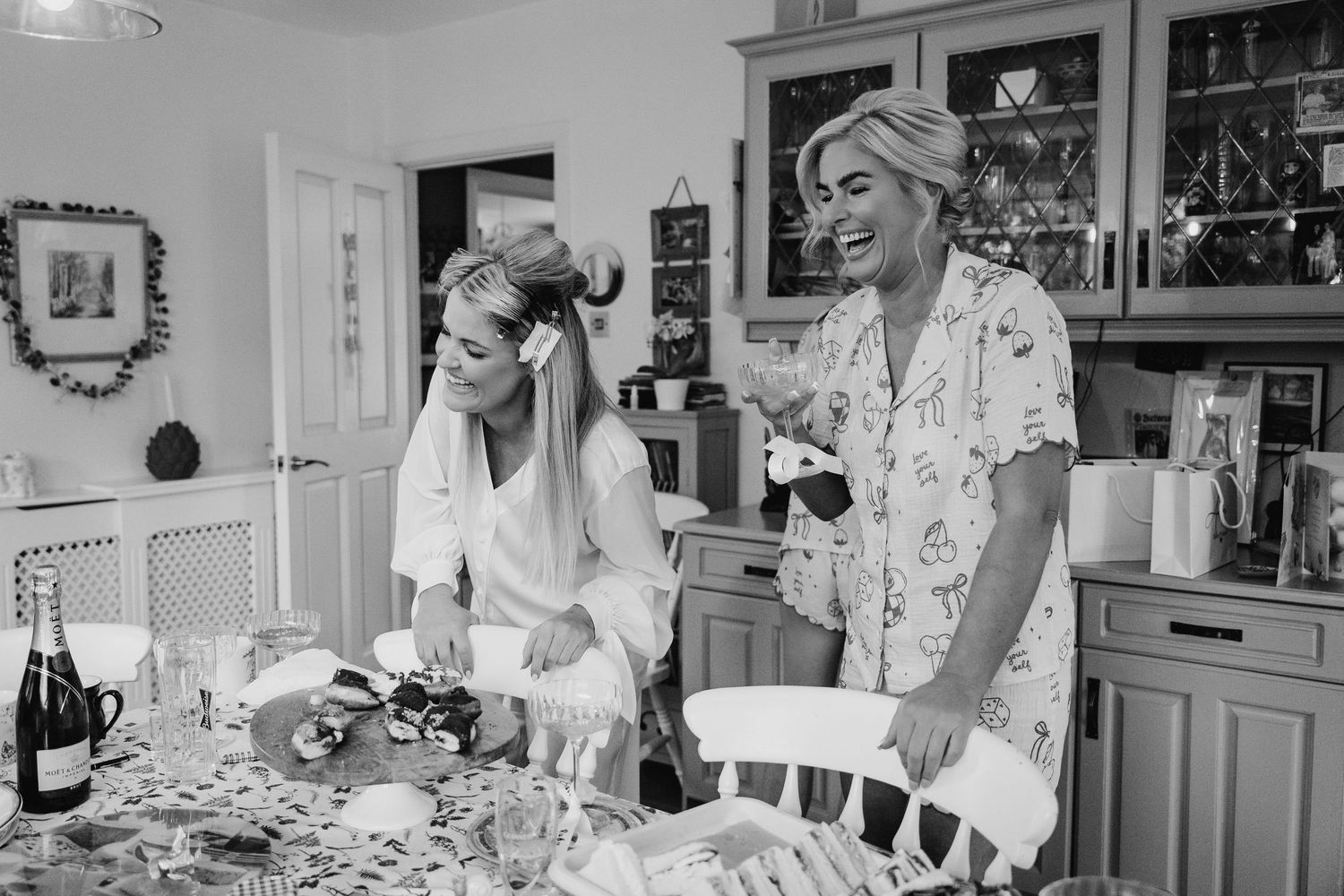 A black and white photo shows two people sharing a laugh while cooking together in a kitchen. The Dean Dublin Wedding Photographer