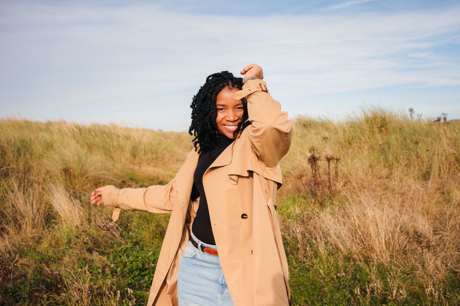 Figure in tan coat stands among dry grass against blue sky backdrop. Dublin professional headshots photographer