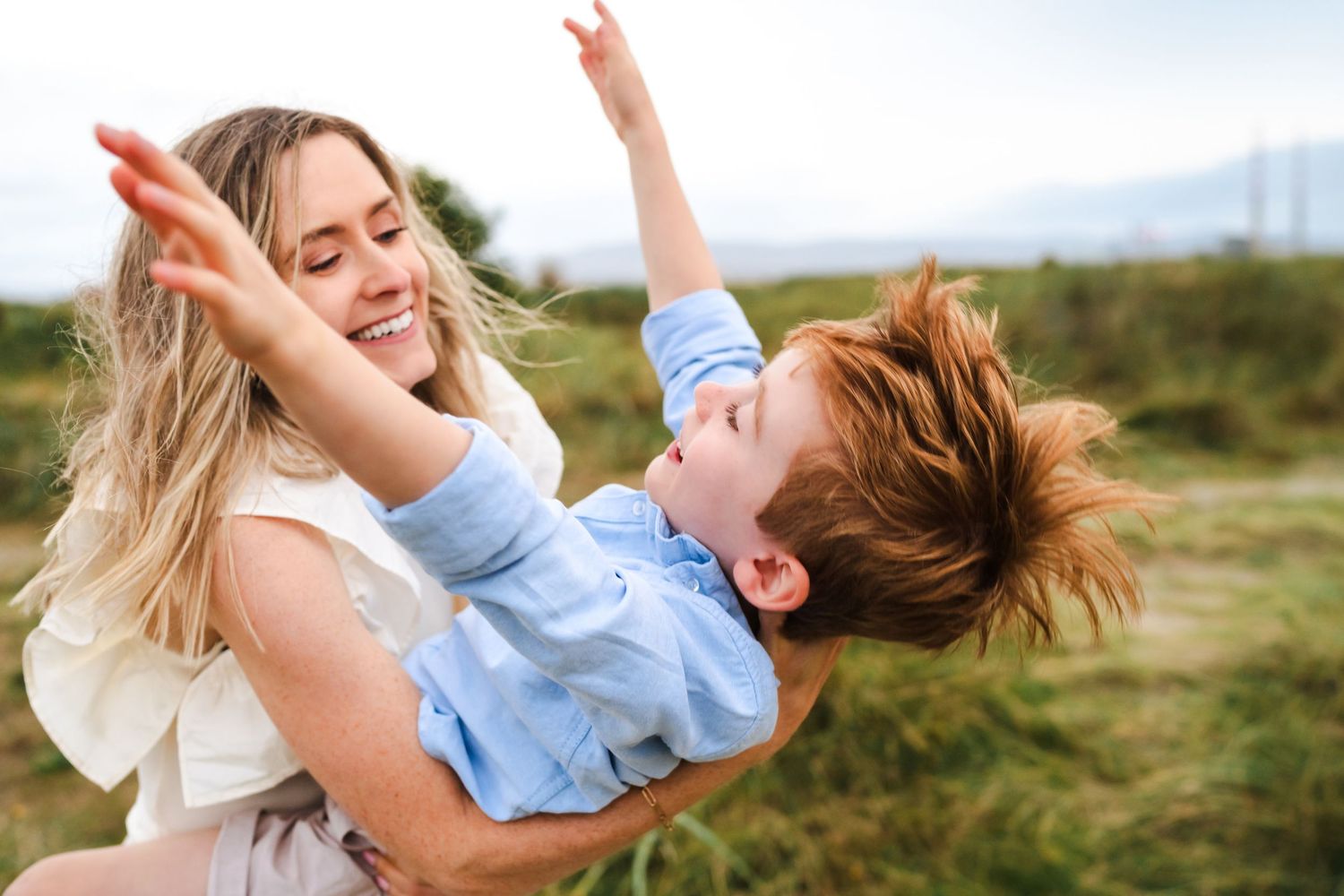 Parent and child playing together outdoors in a grassy field with joyful expressions.  Family photographer Dublin Ireland