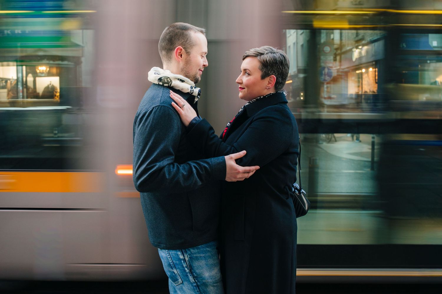 Couple embracing on city street with motion-blurred bus passing in background. family PHOTOGRAPHER Dublin