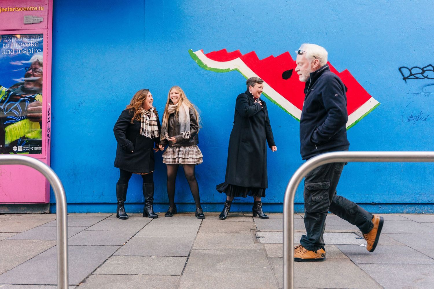 People walking past a bright blue wall with colorful signage in an urban setting.