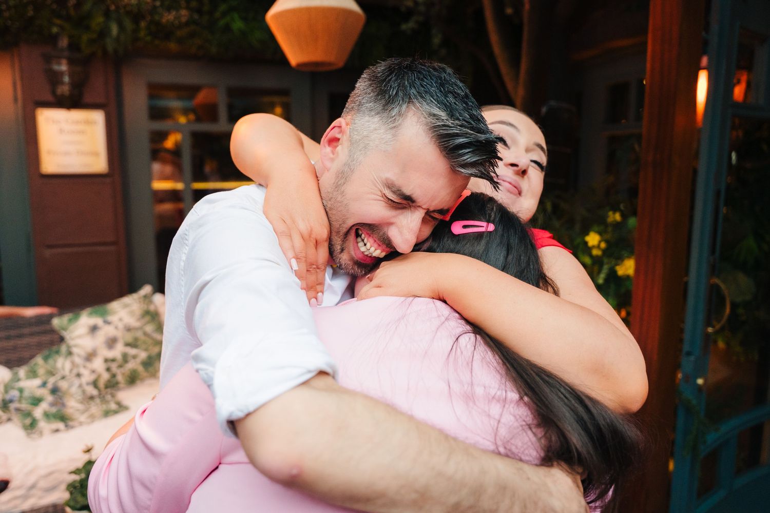 Two people share a joyful embrace and laugh together outside a building entrance at dusk.