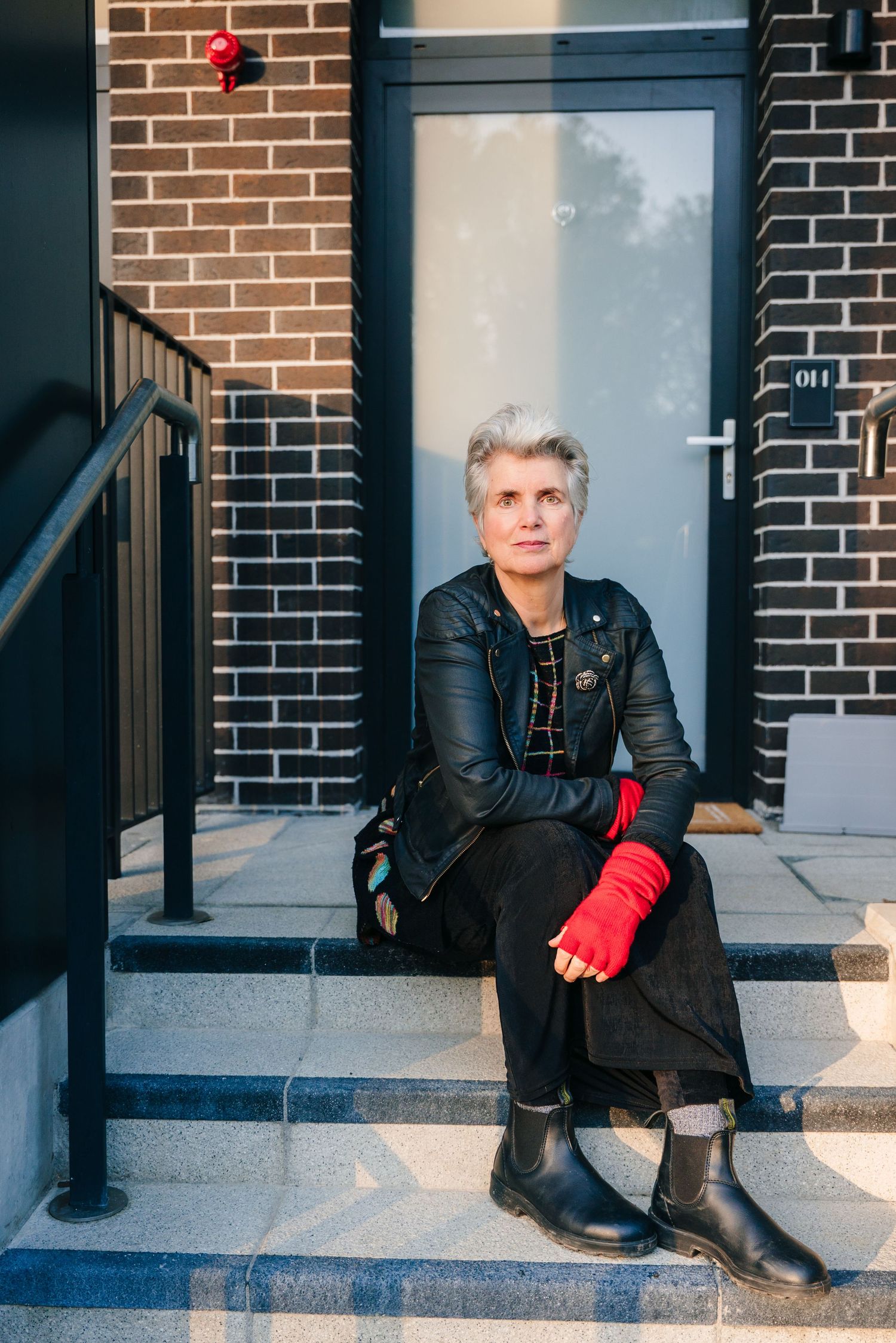 Person in leather jacket and red gloves poses on brick steps in urban setting. professional headshots branding photographer dublin ireland