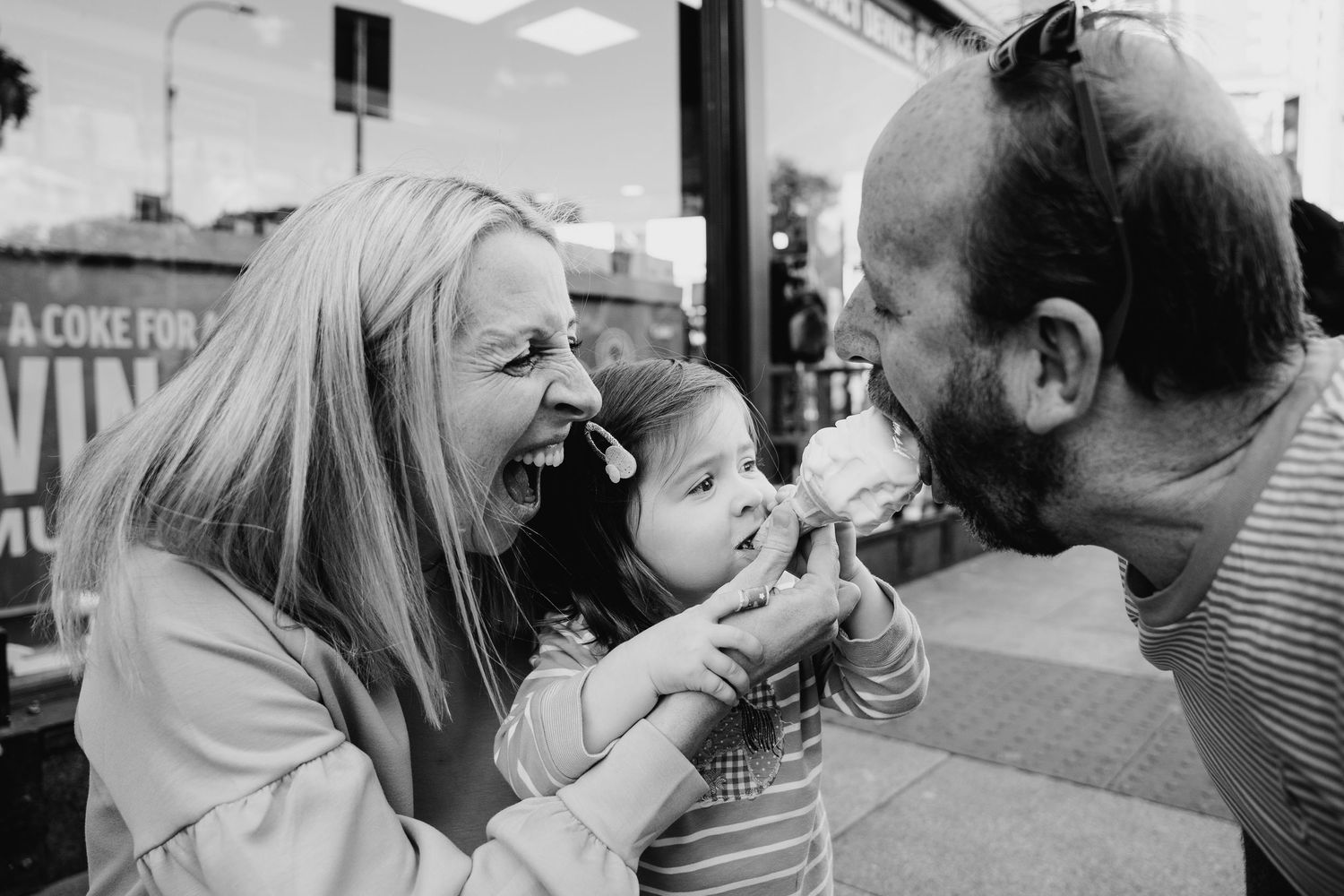 A touching black and white candid photograph shows a joyful family moment with a baby between two adults sharing laughter. family PHOTOGRAPH