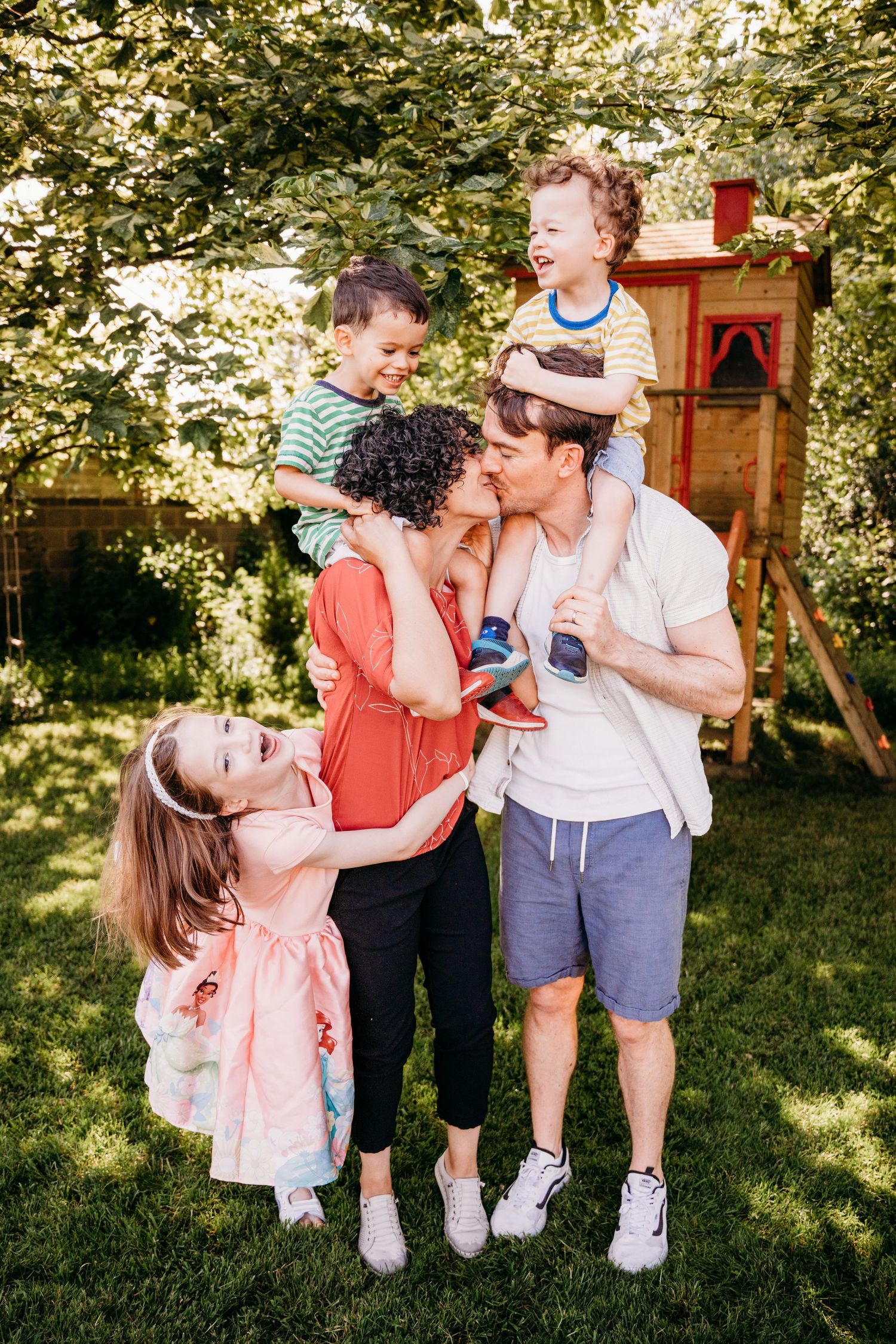 Family having fun together in a sunny backyard with a wooden playhouse visible in the background. Family PHOTOGRAPHER Dublin family PHOTOGRA
