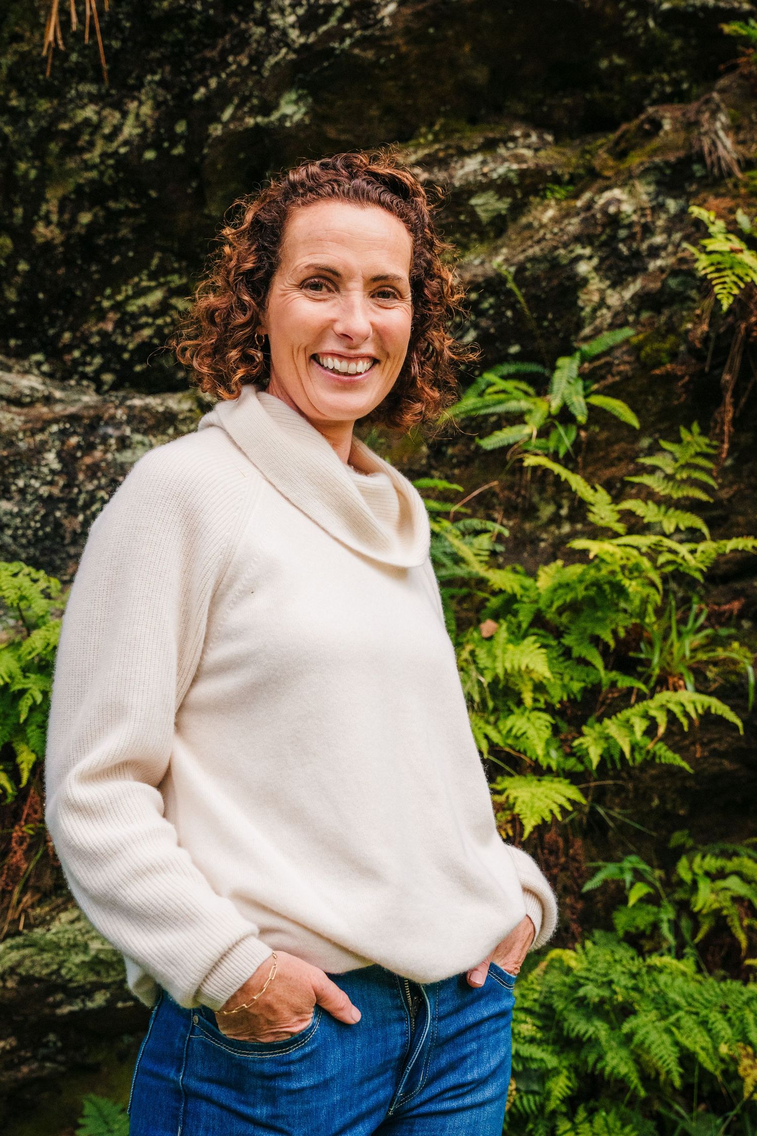 Someone wearing a cozy white sweater poses against a natural backdrop of green ferns and foliage. PHOTOGRAPHER Dublin