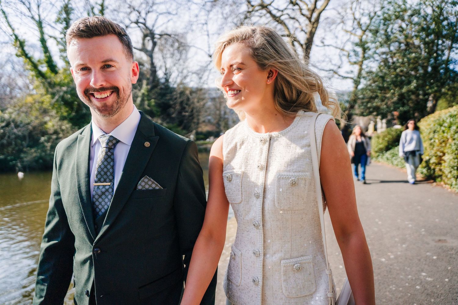 Couple walking together through a sunny park setting with trees in the background. City Hall Dublin wedding photogrAPher