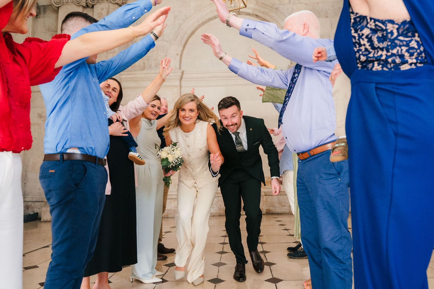 Wedding party creates tunnel arch with arms while couple walks through center. City Hall Dublin wedding photogrAPher