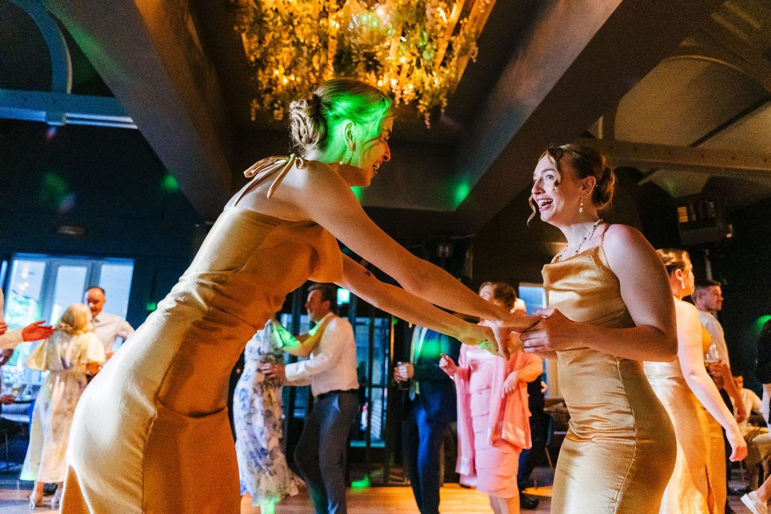 Poulaphouca Wedding photographer wicklow  Party guests in matching champagne-colored dresses dance energetically under ornate chandeliers.