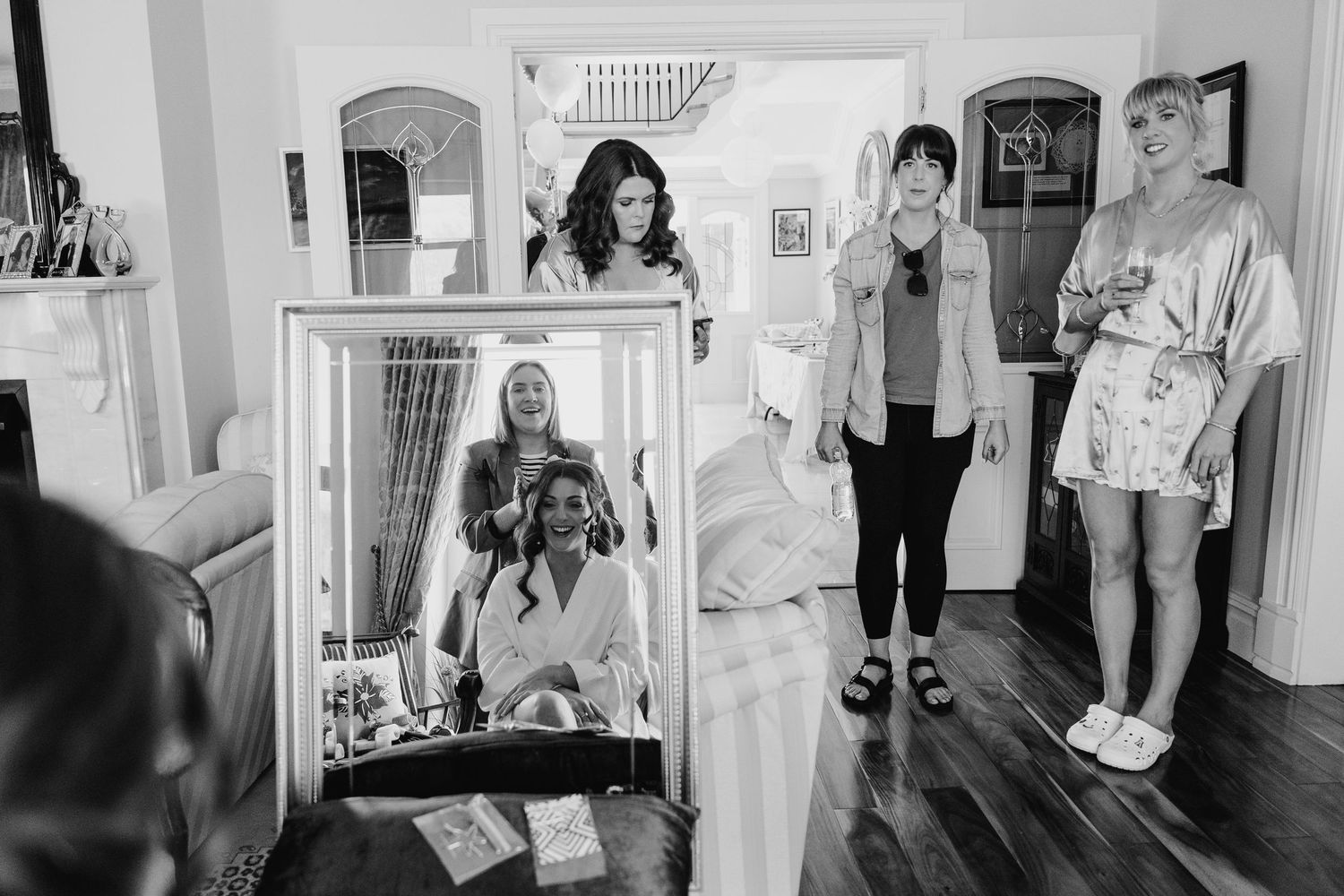 Black and white photo of group preparing in room with large mirror and hardwood floors. Castle Leslie Wedding Photographer Dublin