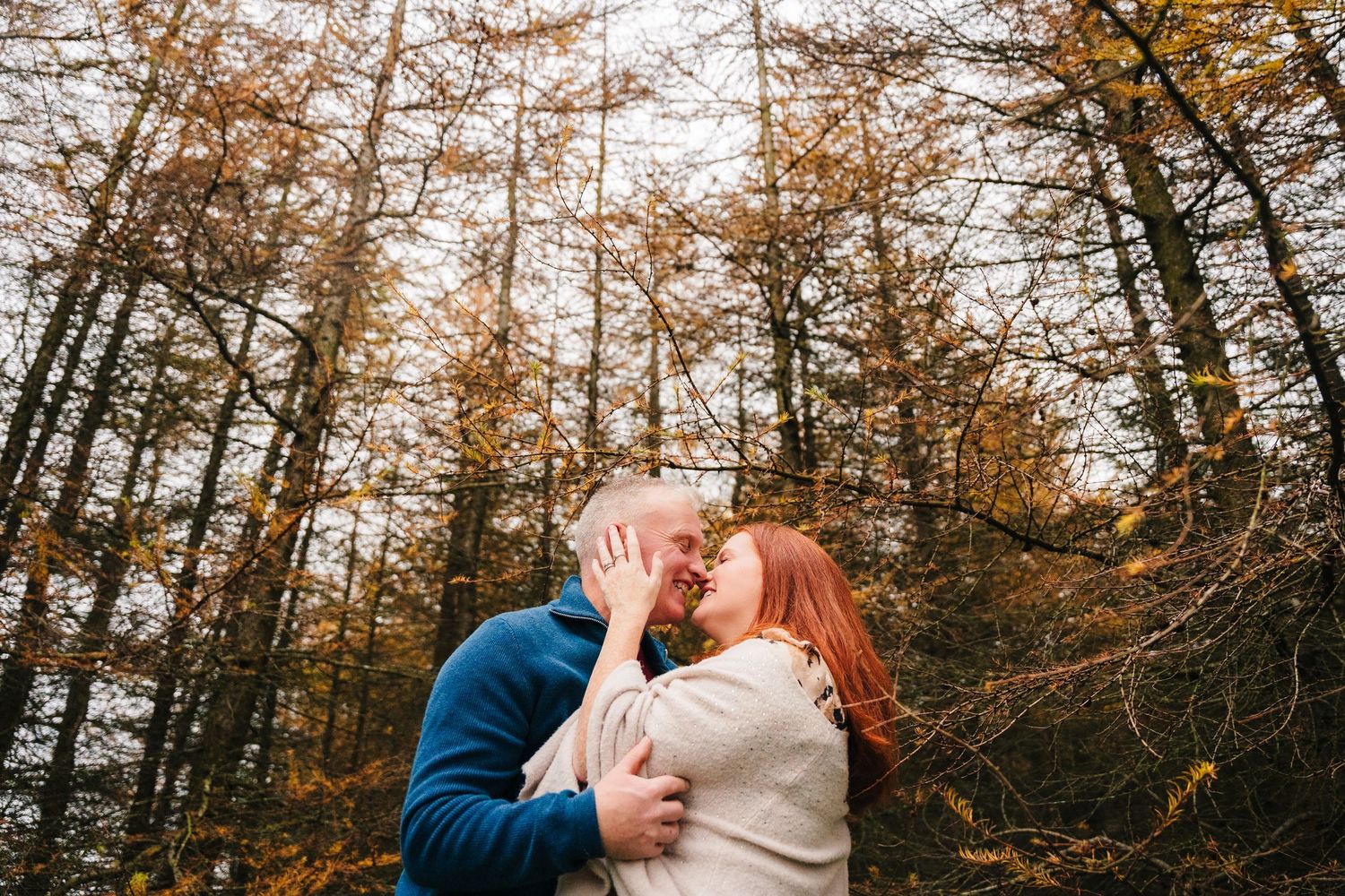 A couple sharing a romantic moment among autumn-colored trees in a forest.