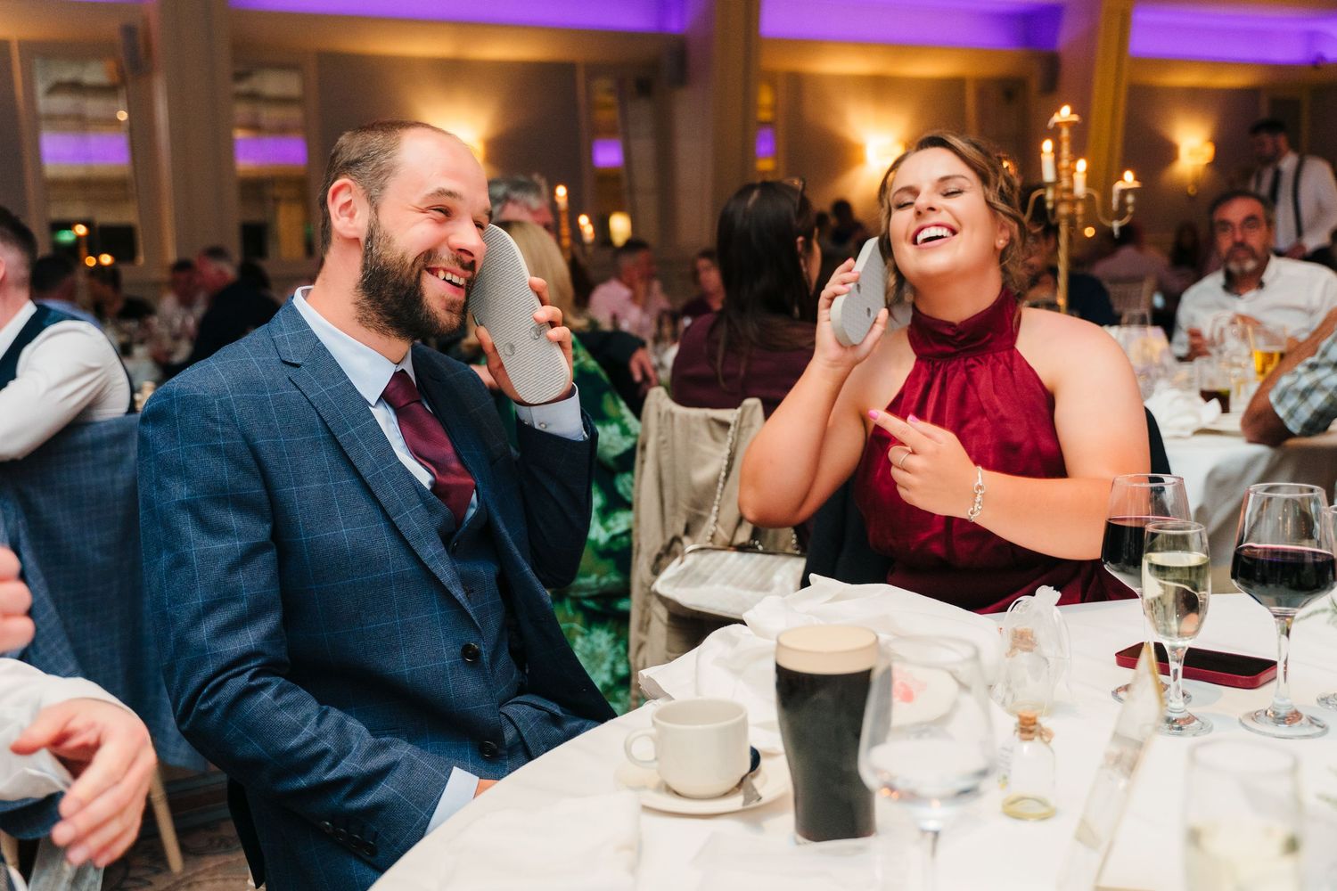 Wedding guests share a laugh together at their table during the reception with drinks and candles visible. Wedding PHOTOGRAPHER Dublin