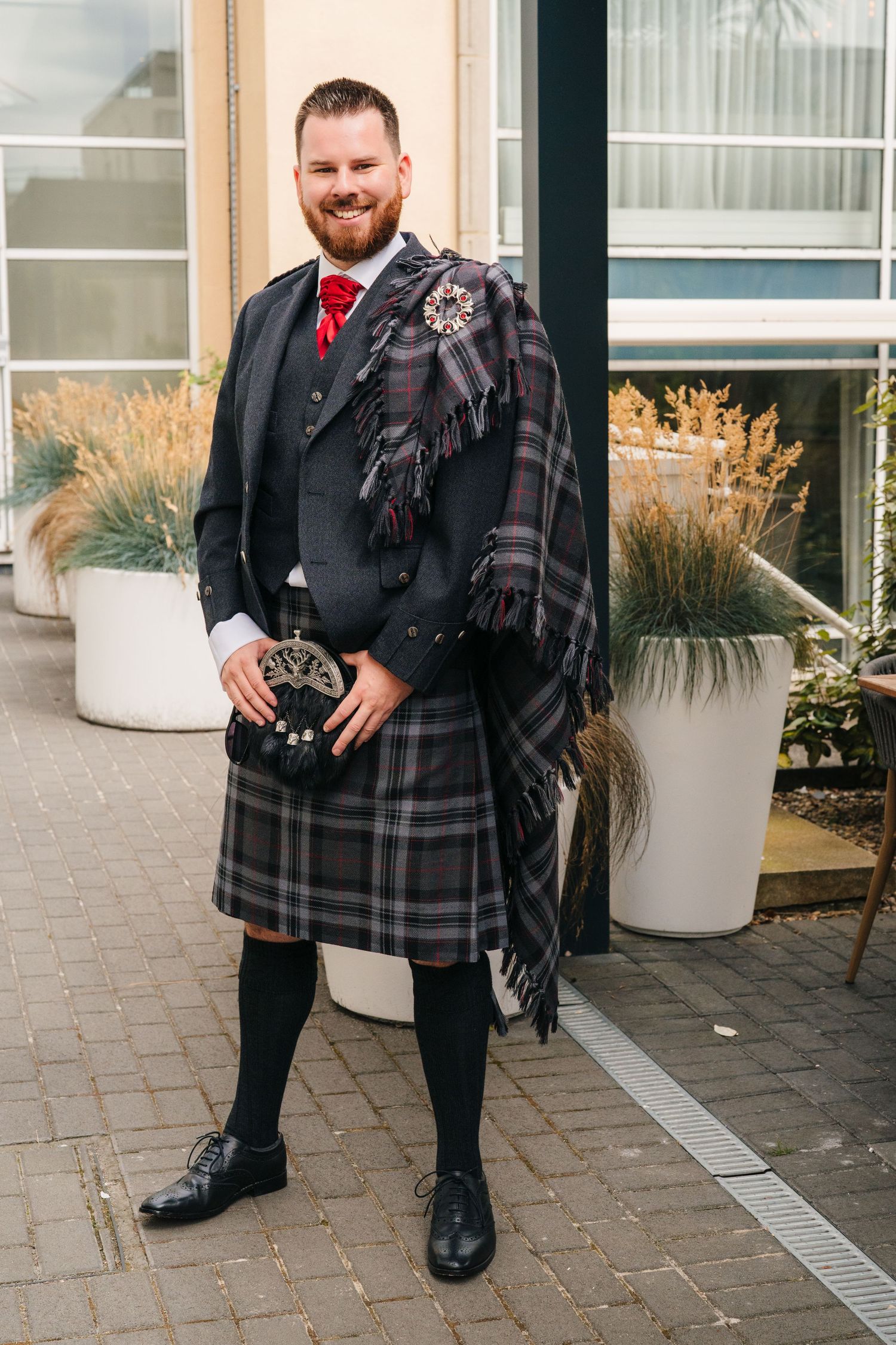 Scottish themed wedding attire featuring a black suit with plaid kilt and red accents. Portmarnock Hotel Wedding PHOTOGRAPHER Dublin