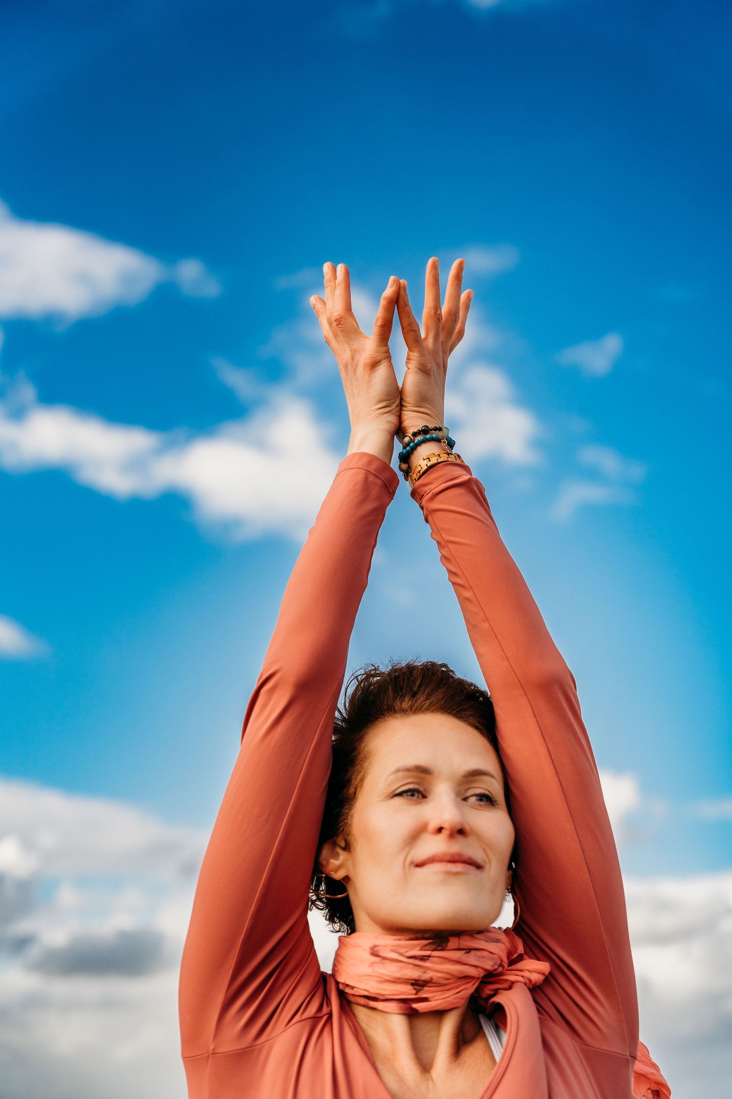 Person in coral colored top reaching upward against vibrant blue sky with white clouds in a series of poses. Portrait PHOTOGRAPHER Dublin