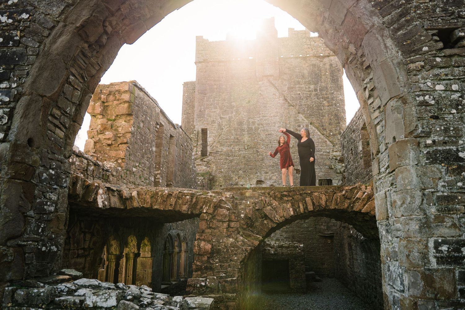 Sunlight streams through castle ruins as people explore the ancient stone architecture. Family PHOTOGRAPHER Dublin