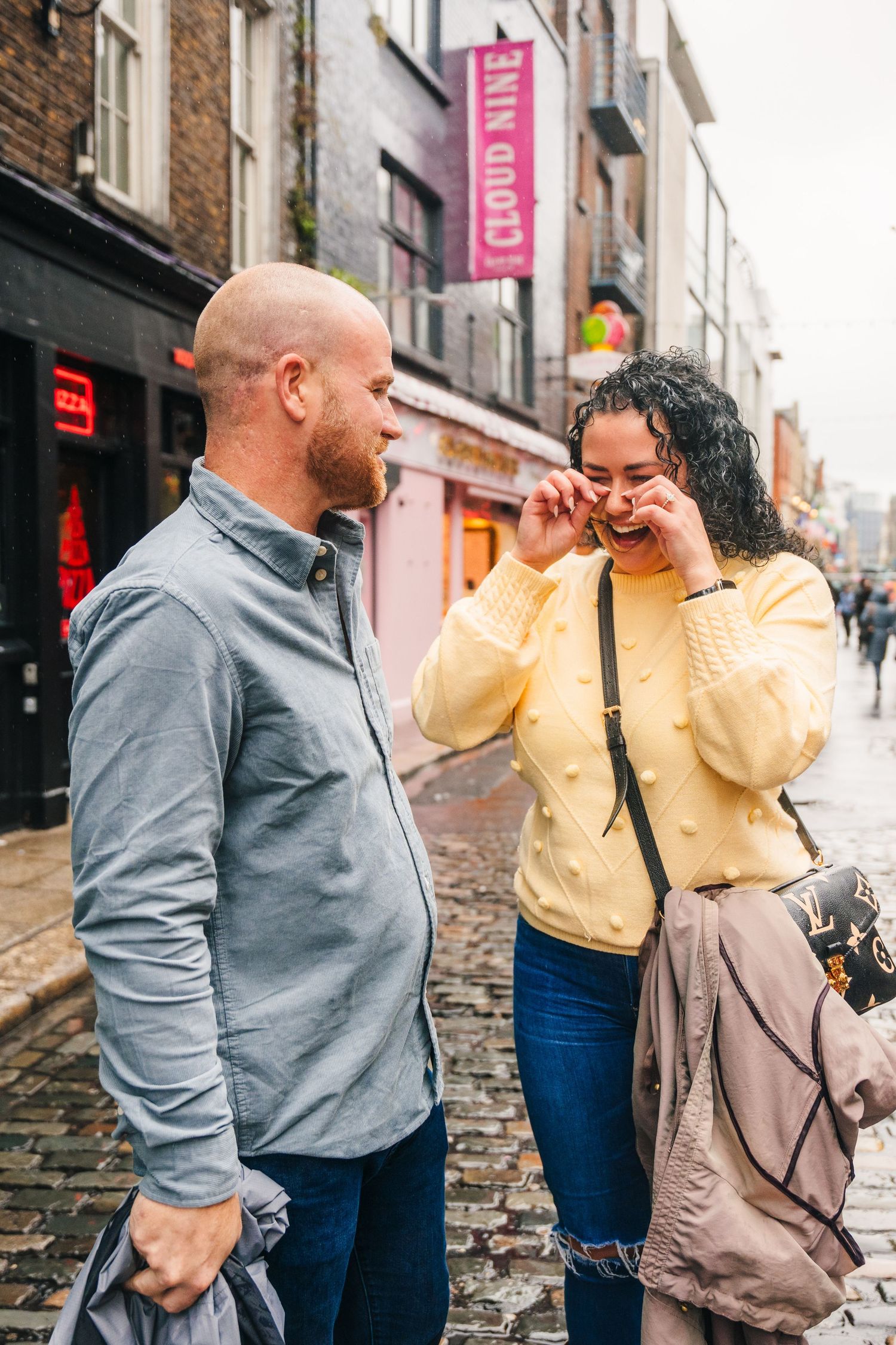 Couple laughing and sharing joyful moments together on a city street in front of brick buildings. Proposal Dublin Photographer