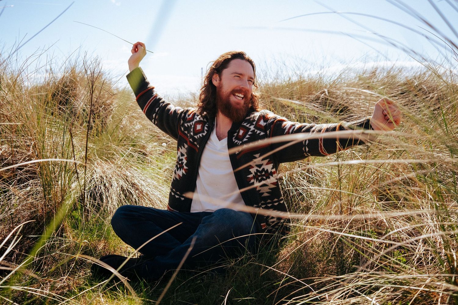 Musician in floral jacket expressing joy while sitting in tall grass on a sunny day. PHOTOGRAPHER Dublin