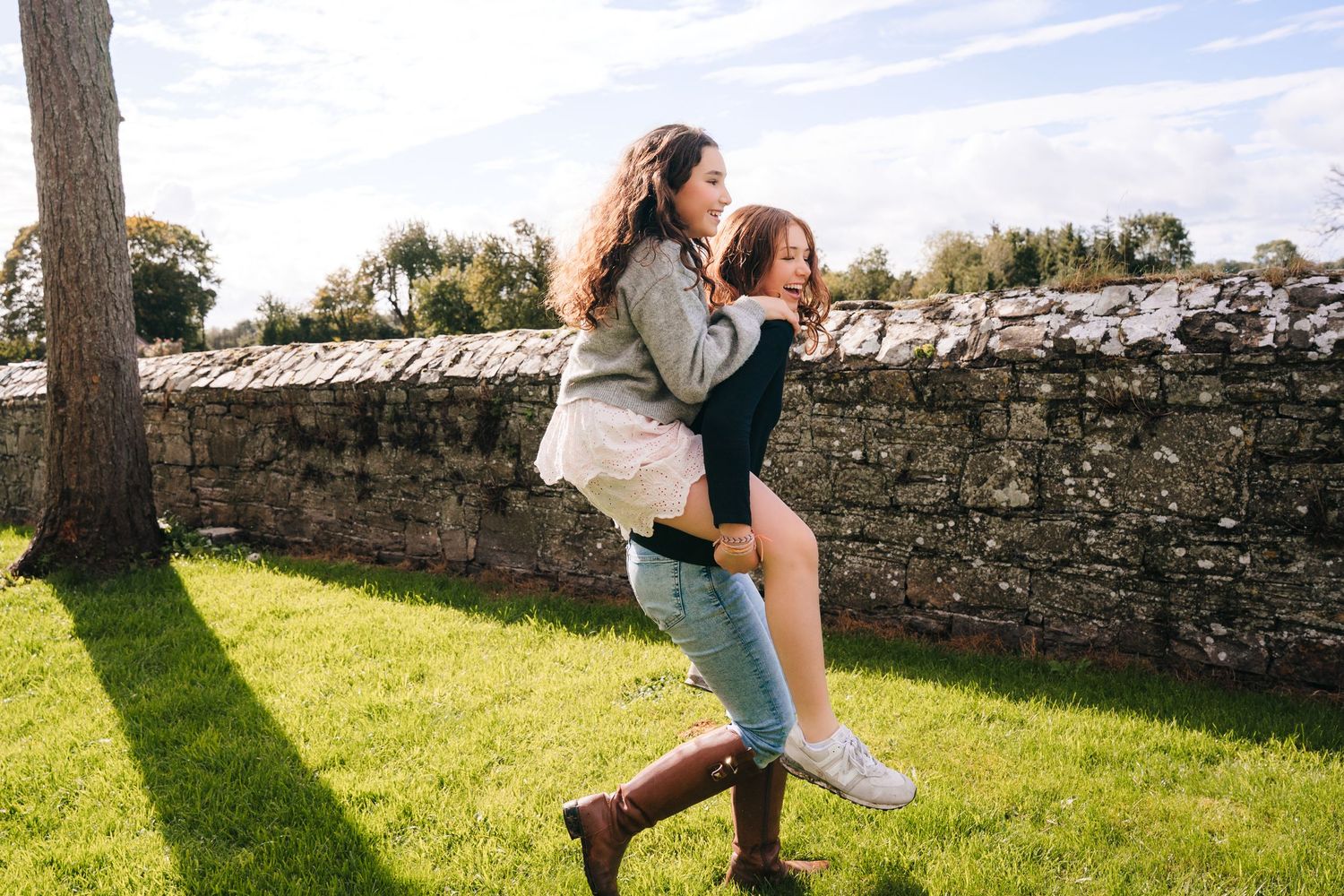 Playful moments captured in a grassy field beside old stone walls on a sunny afternoon. BEctive abbey family photographer dublin