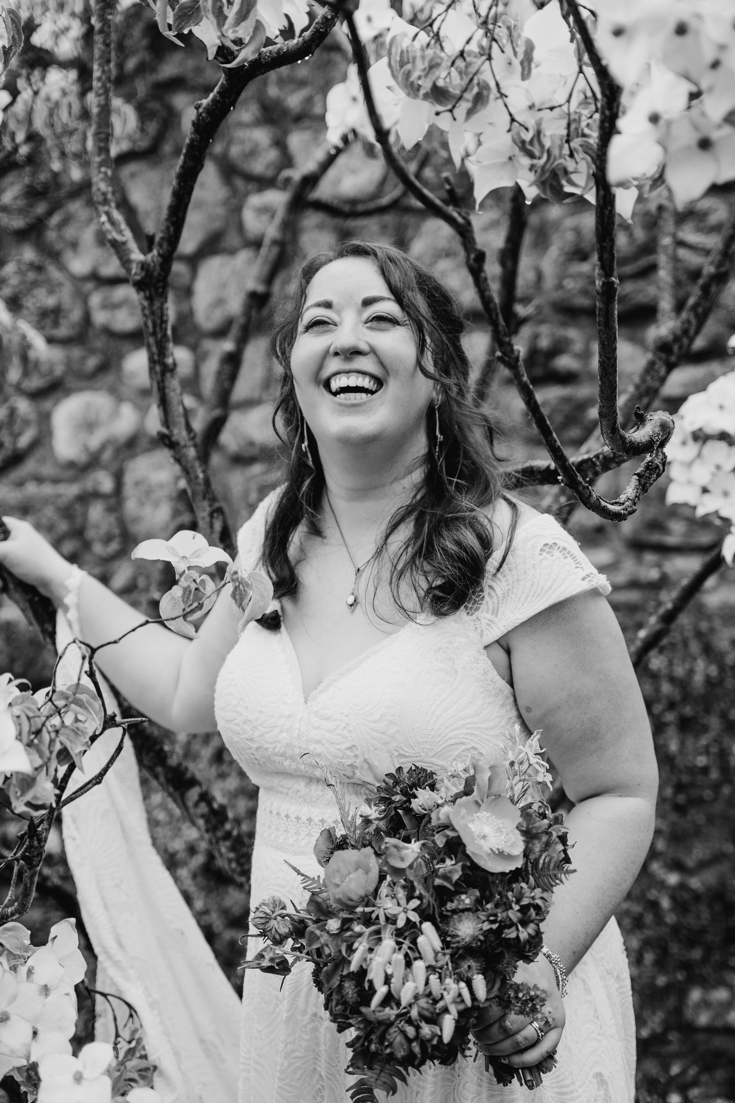Black and white portrait of a joyful bride holding her bouquet against a stone wall. Wedding photographer Dublin