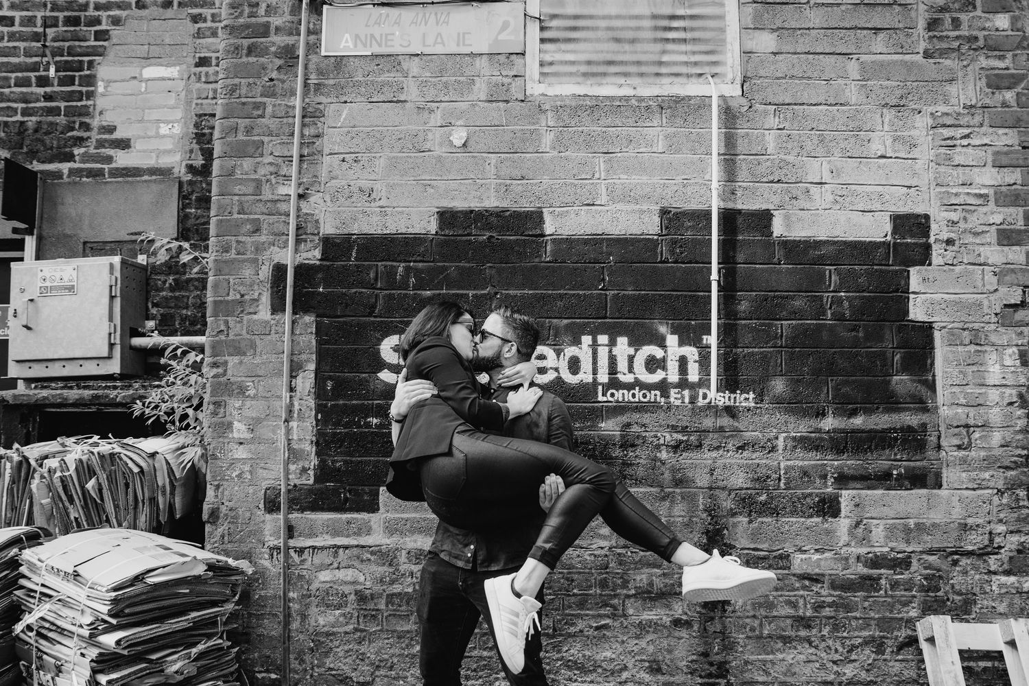 Black and white photo shows two people embracing in front of a brick wall with the text 