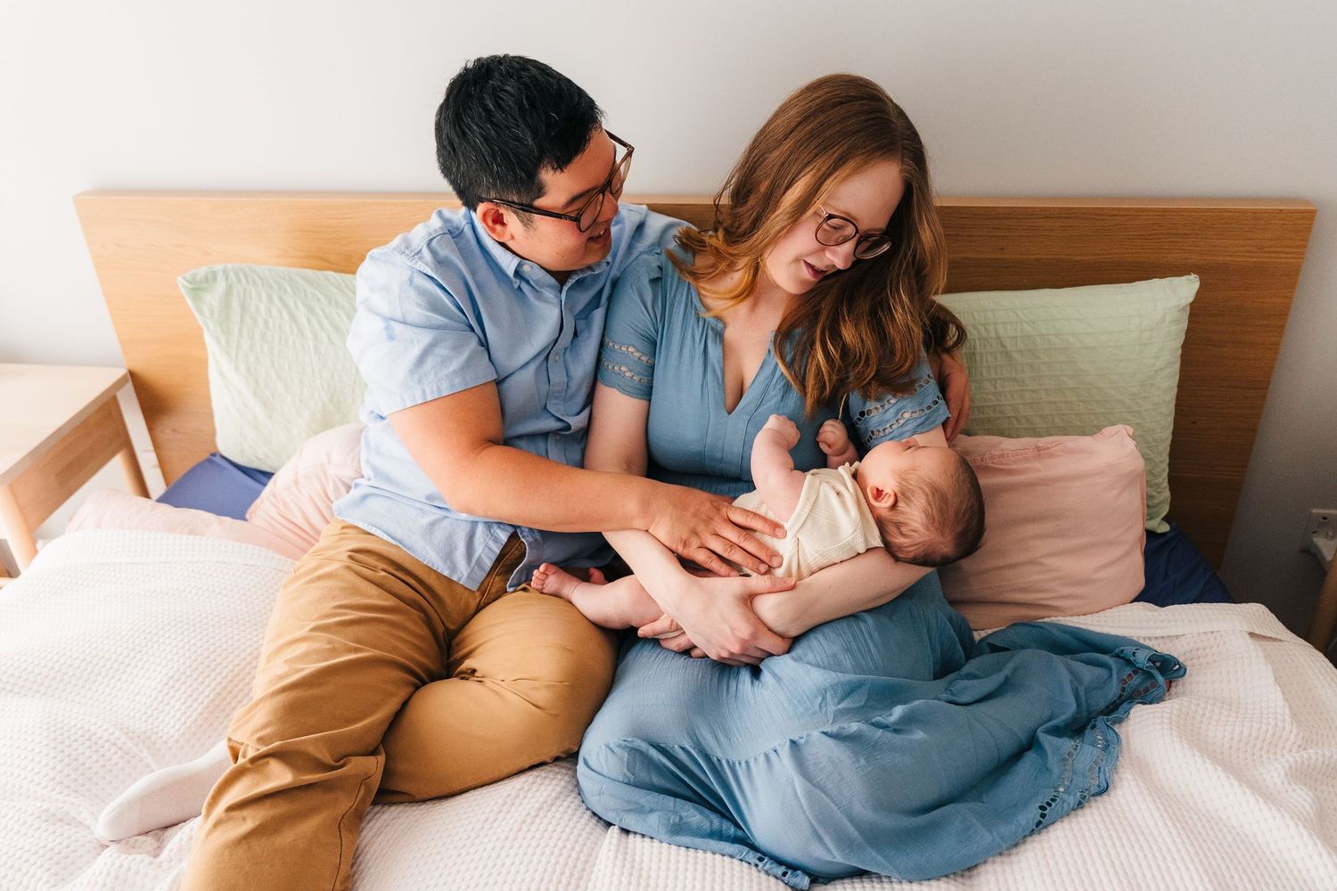 Parents spend intimate time with newborn baby while relaxing together on cozy bed with pillows and blankets. family PHOTOGRAPHER Dublin