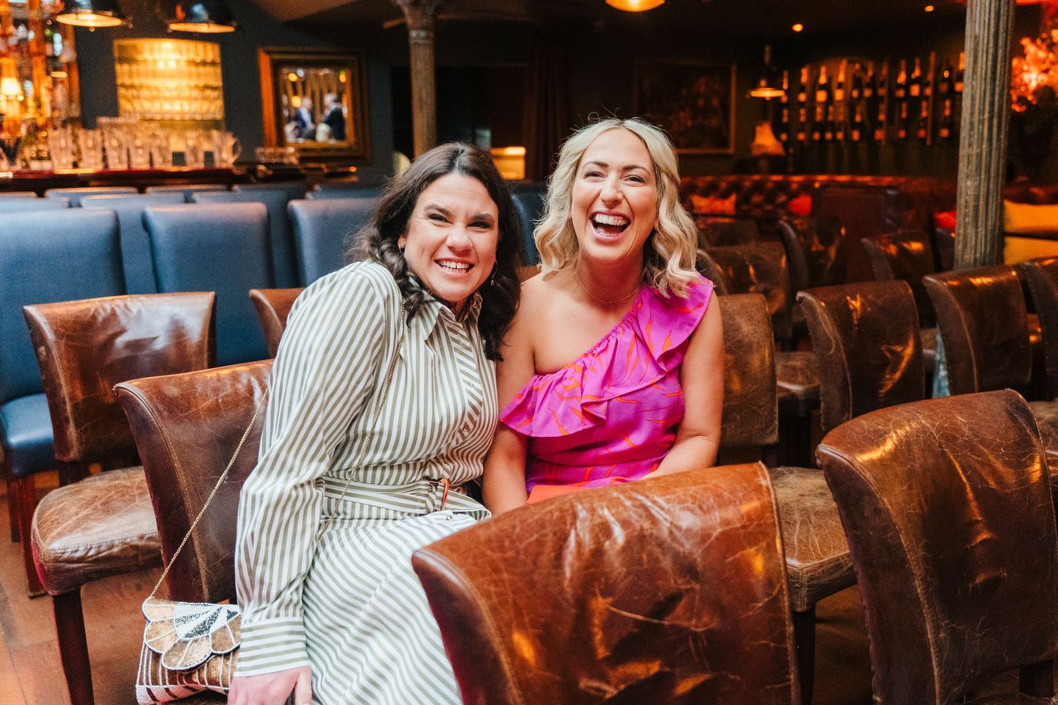 Friends laughing together while seated at a bar with brown leather chairs. Marco Pierre Dublin Wedding Photographer