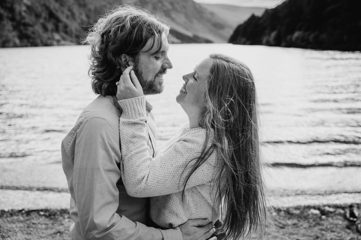 A romantic black and white candid photo of a tender moment between a couple by a lake in the mountains. PHOTOGRAPHER Dublin ireland
