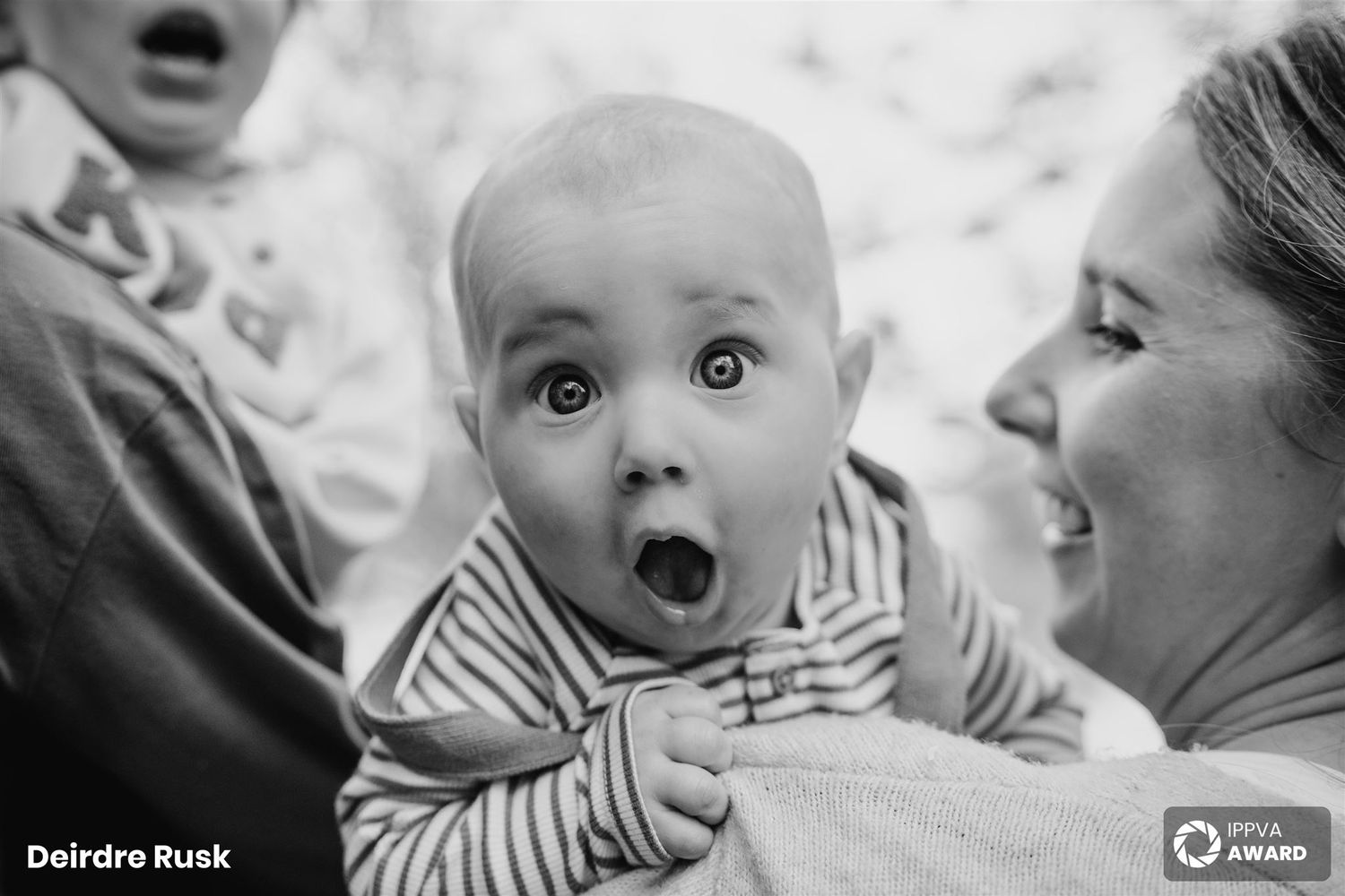 Black and white portrait of an expressive baby showing surprise while being held. Family PHOTOGRAPHER Dublin PHOTOGRAPHER Dublin
