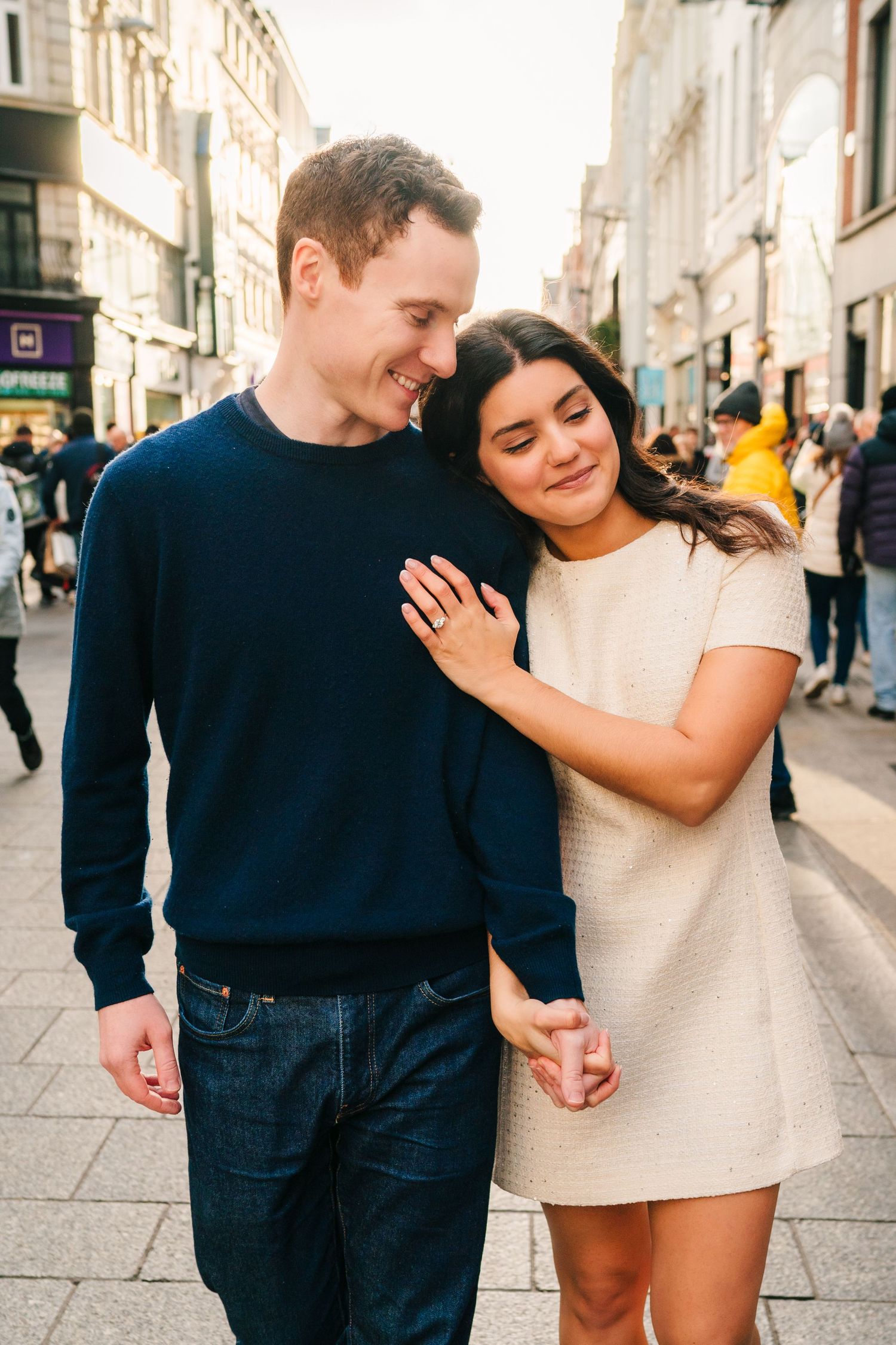 A couple walking together and embracing on a European city street with historic buildings in the background.