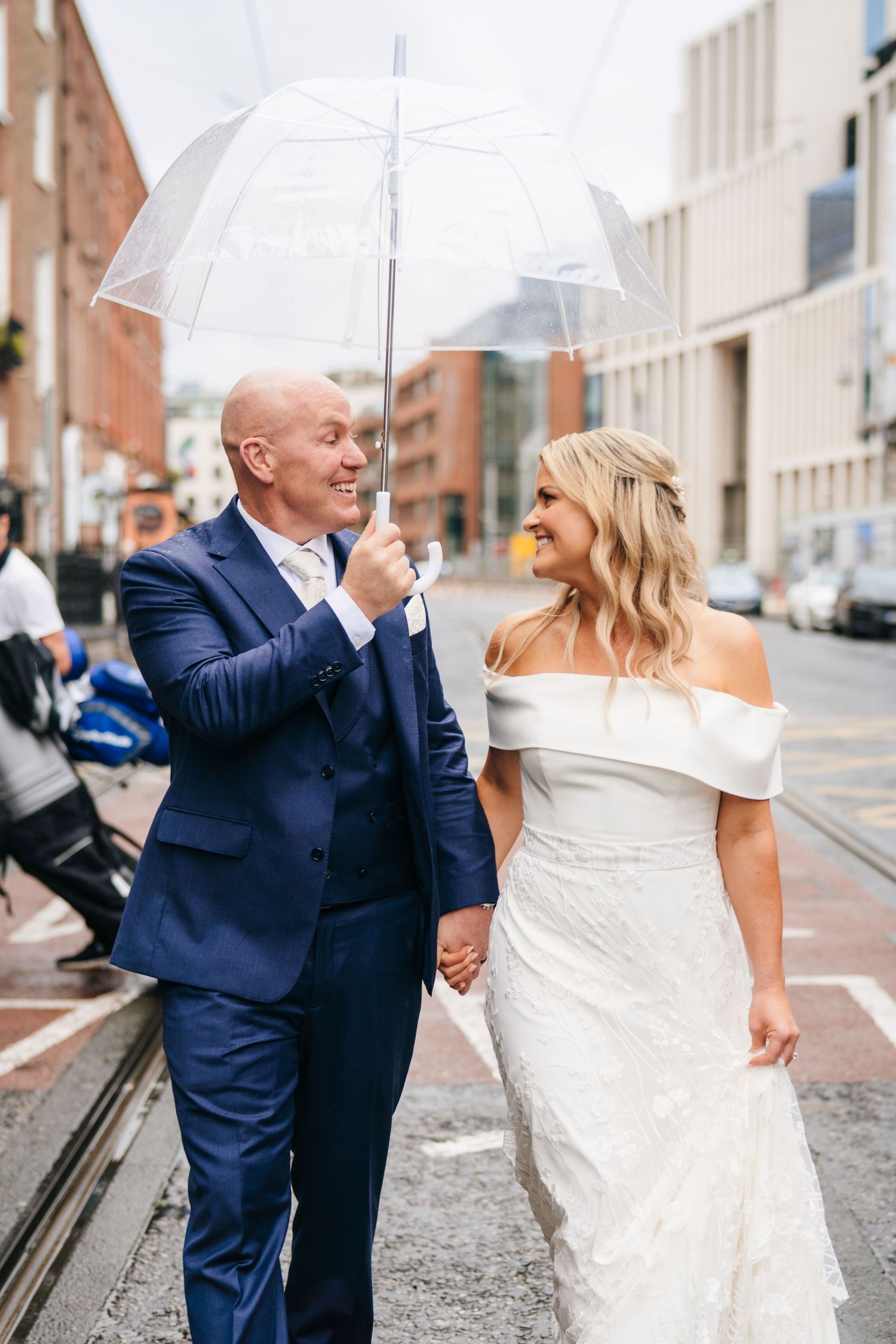 Happy couple walking on a rainy city street sharing an umbrella on their wedding day. The Dean Dublin Wedding Photographer
